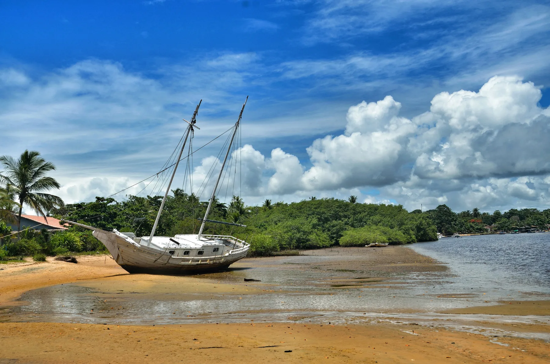 Barco parado na areia da barra do rio Caraíva, com coqueiral ao fundo