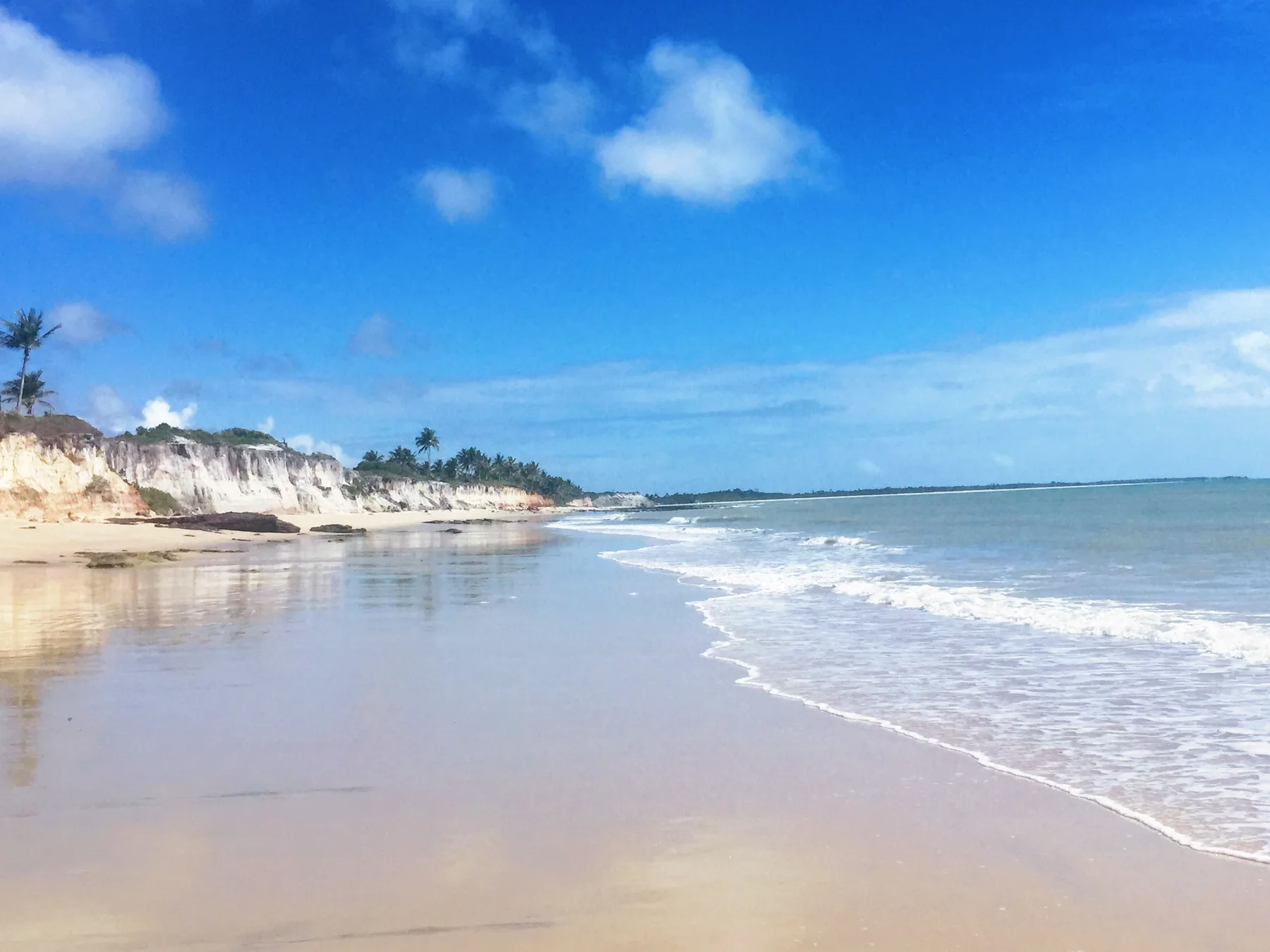 Faixa larga de areia na maré baixa, entre o mar e as falésias