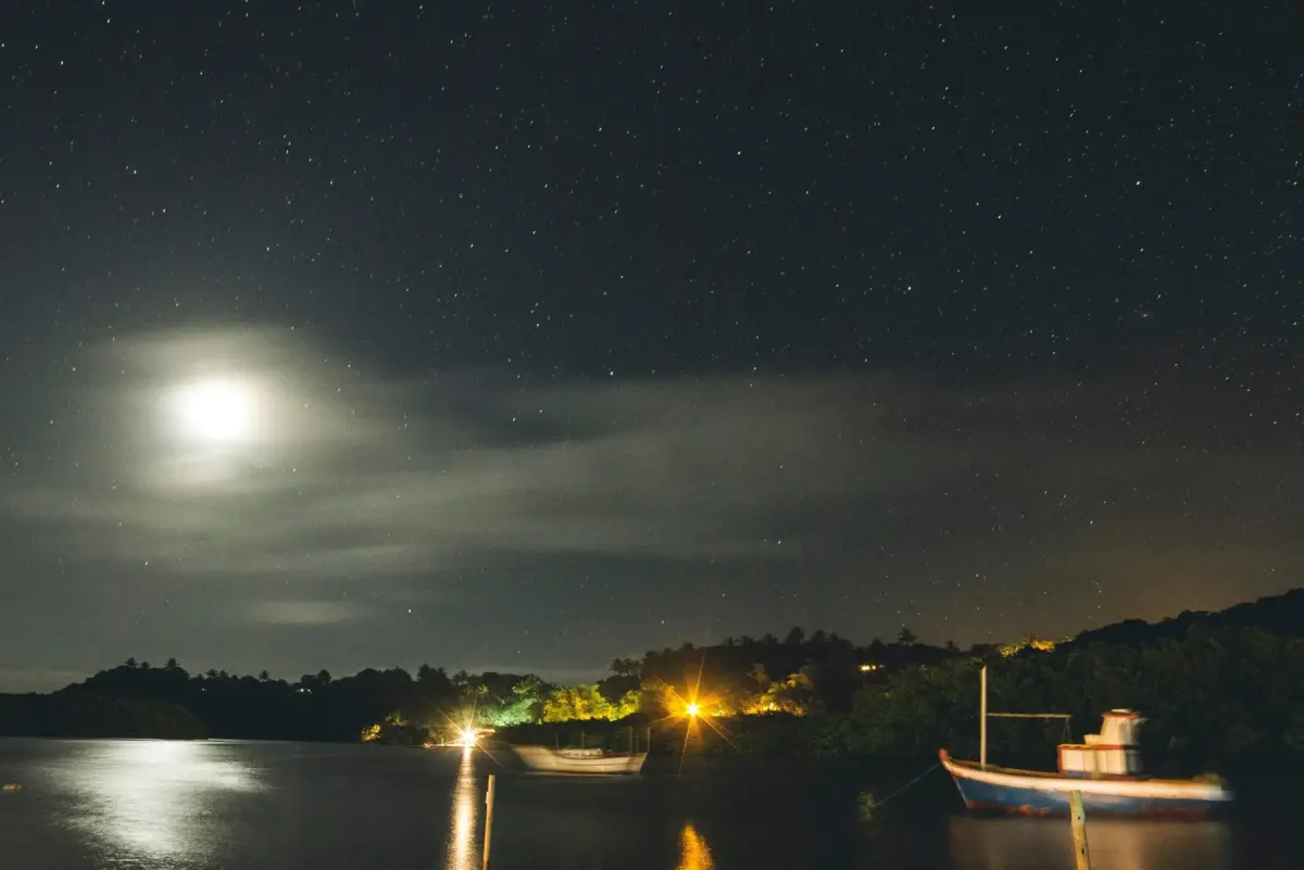 Rio Caraíva à noite, com a lua refletida na água e as luzes da vila ao fundo