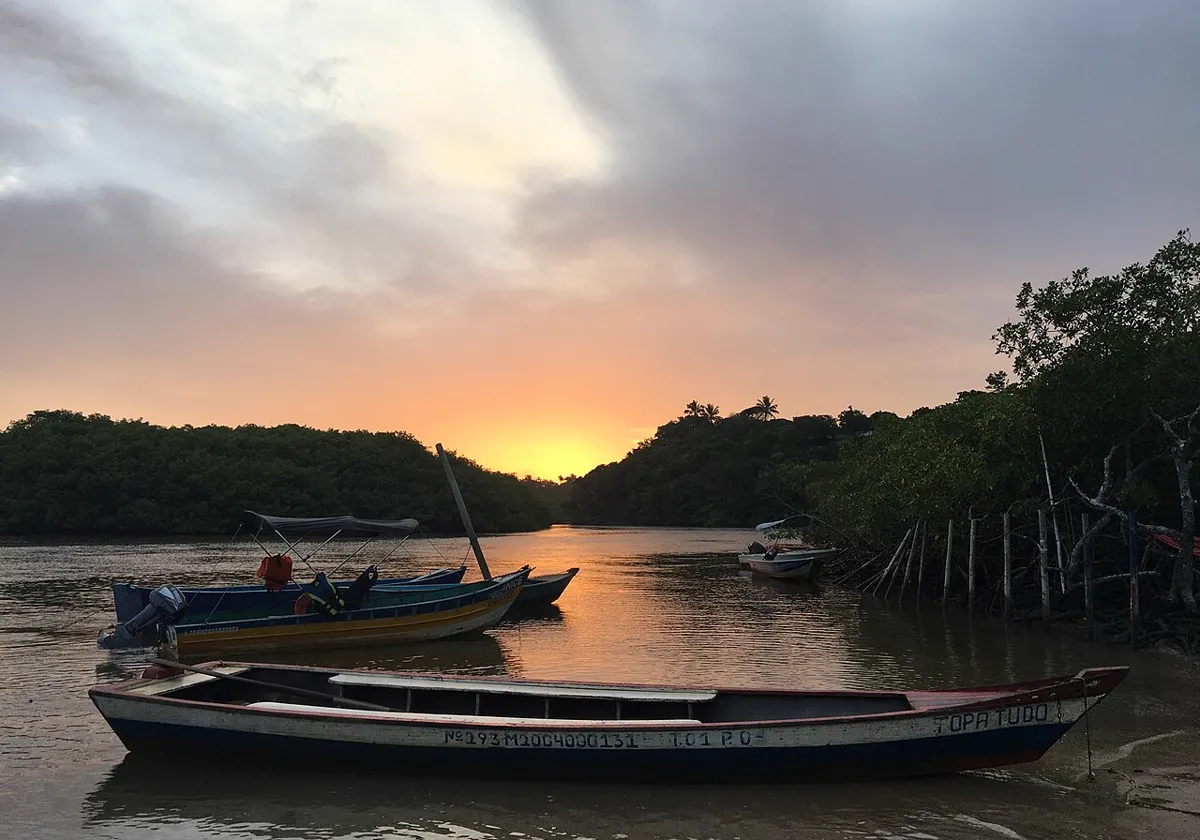 Pôr do sol no rio Caraíva, com o sol baixando entre a mata e canoas ancoradas na água